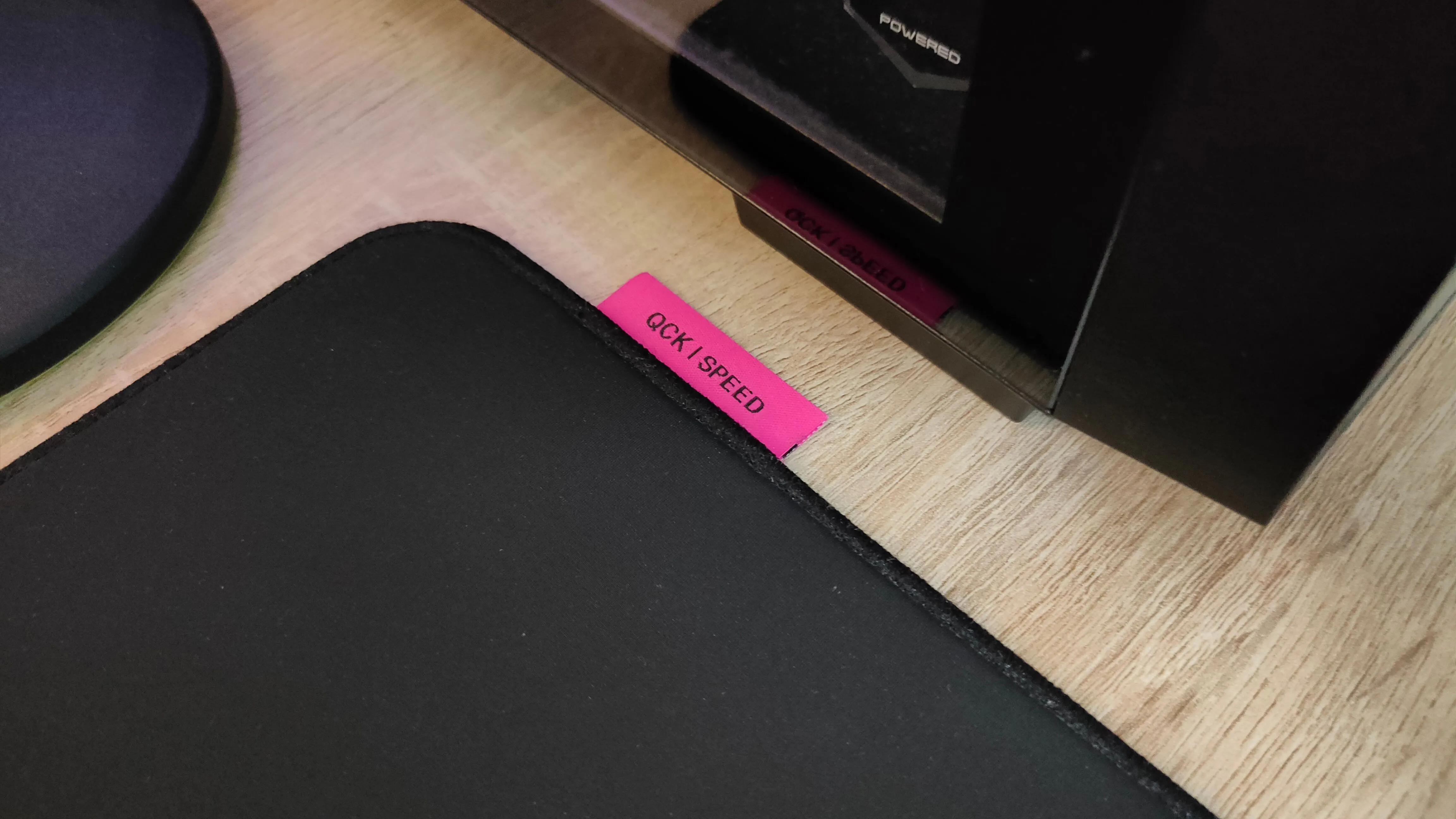 Cận cảnh logo QCK Performance Speed màu hồng trên góc thảm lót chuột SteelSeries, biểu tượng của dòng sản phẩm tối ưu tốc độ