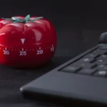 Đồng hồ hẹn giờ Pomodoro hình quả cà chua bên cạnh laptop giúp tăng tập trung