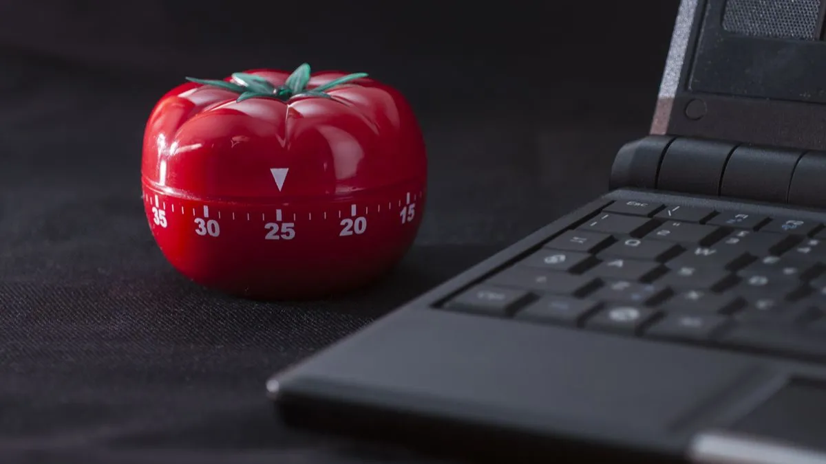 Đồng hồ hẹn giờ Pomodoro hình quả cà chua bên cạnh laptop giúp tăng tập trung