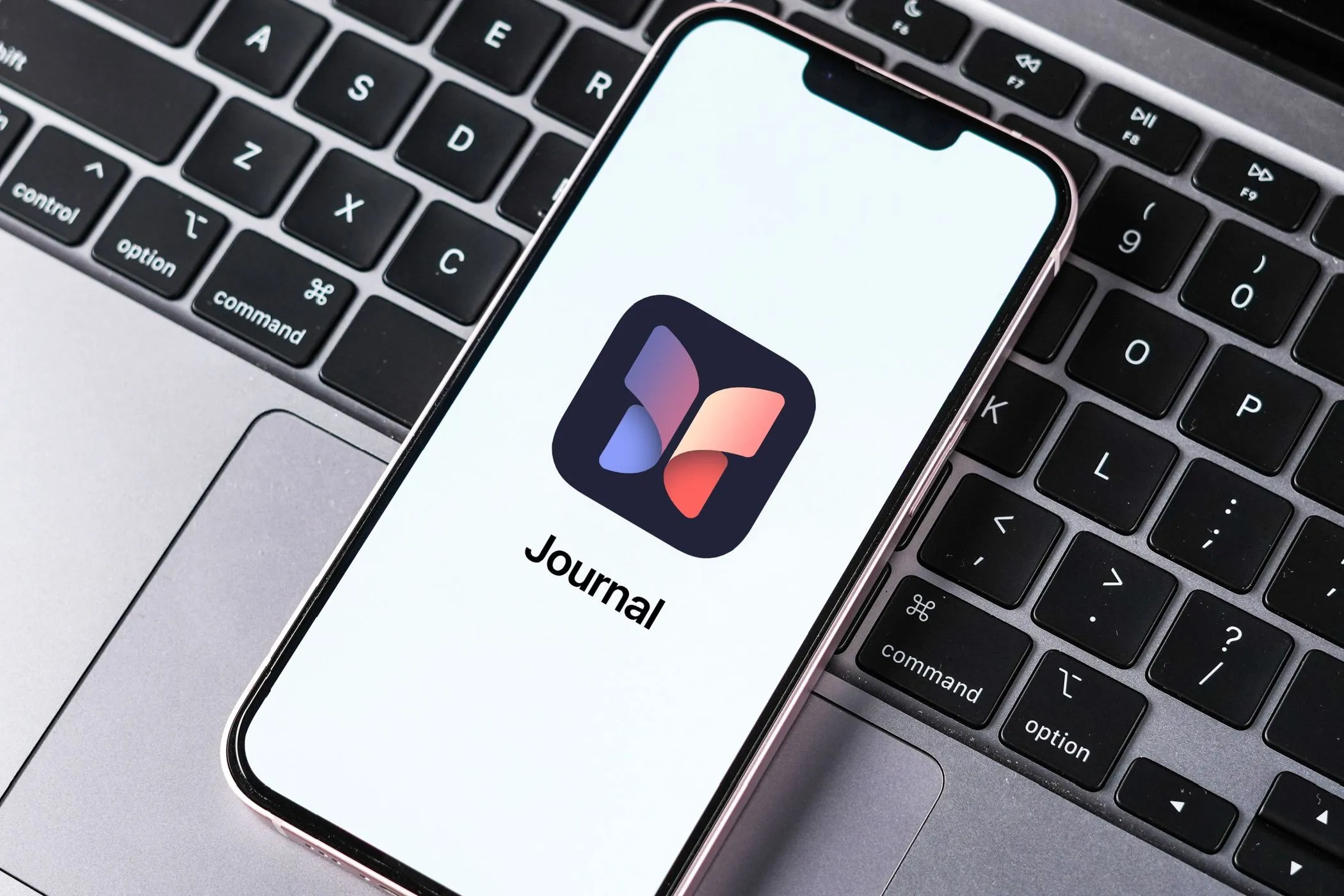 Giao diện ứng dụng Nhật ký (Journal) của Apple trên màn hình iPhone đặt trên bàn phím MacBook.