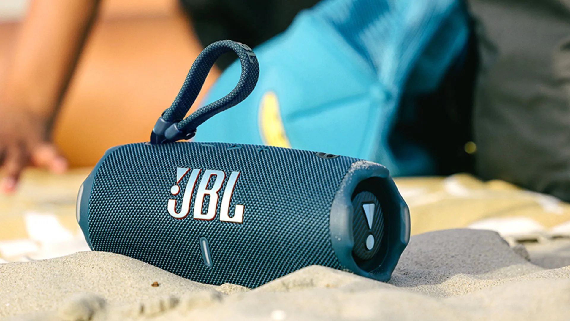 Loa JBL Charge 6 màu đen đặt trên bãi cát với sóng biển ở phía sau, sẵn sàng cho những chuyến đi mùa hè