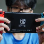 Một người đàn ông đang chơi game trên máy Nintendo Switch cầm tay, tận dụng thời gian rảnh khi đi du lịch.