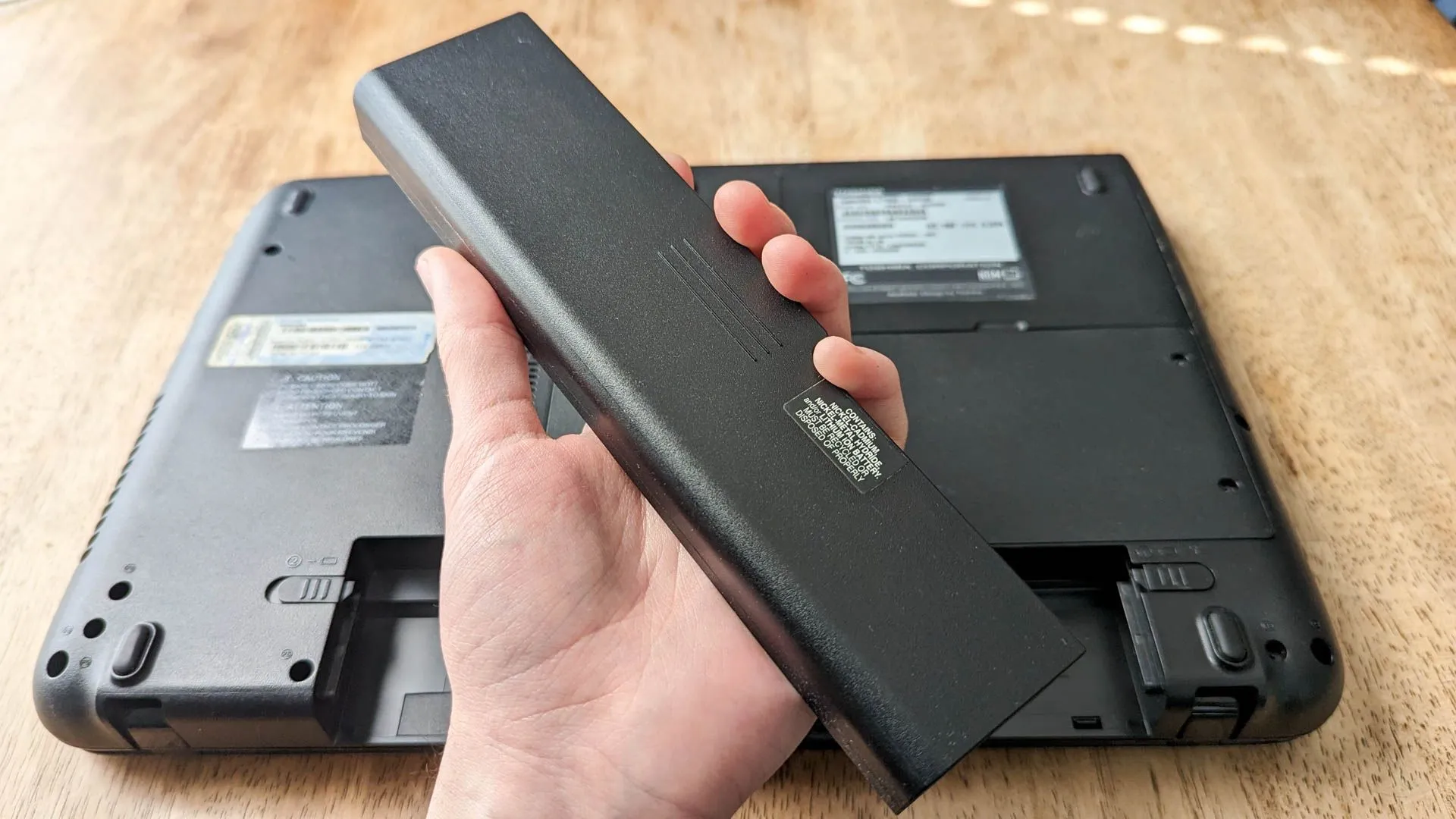 Một người đang cầm pin laptop rời, minh họa khả năng thay thế hoặc kiểm tra pin
